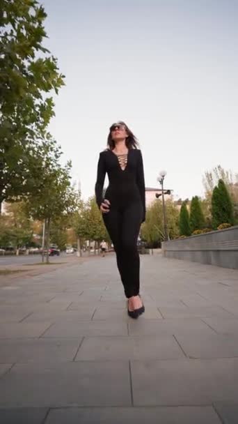 穿着黑色紧身衣 头戴皮夹克 步履蹒跚 步履蹒跚 头戴黑色紧身衣的有诱惑力的瘦女人 沿着城市街道走着 时尚与美的概念 垂直录像 慢动作 — 图库视频影像