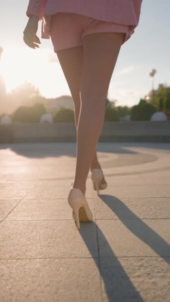 穿着高跟鞋的瘦腿优雅地沿着城市街道行走 有诱惑力的女人在日落时穿过城市公园 垂直录像 慢动作 — 图库视频影像