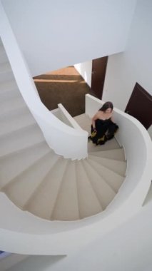 Kafasında taçla fantastik bir güzellik kraliçesi ve altın desenli güzel siyah elbiseli kadın lüks beyaz merdivenlere tırmanıyor. Moda Modeli Görüntü Tarihi Kraliçesi Pozisyonunda. Dikey Görünüm, Üst Görünüm