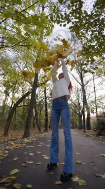 Slim Happy Woman in a White Sater and Jeans is up a Umbrella which Yellow Autumn Leaves are Flying. Yavaş Hareket, Dikey Video.