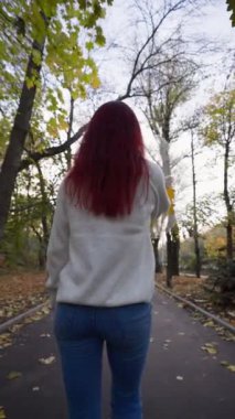 Arka Manzara, Beyaz Kazaklı Mutlu Bir Kadın Sonbahar Yapraklarının Uçuştuğu Şemsiyeyle Yürüyor. Yavaş Hareket, Dikey Video.