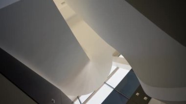 Minimalist bir iç mekanda kıvrımlı bir tarzda güzel, lüks, beyaz bir merdiven. Yavaş çekim, alt açı.