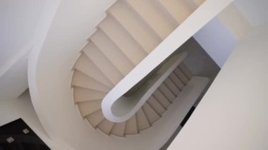 Minimalist bir iç mekanda kıvrımlı bir tarzda güzel, lüks, beyaz bir merdiven. Yavaş çekim, üst görünüm.