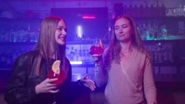 İki Kız Arkadaş Bir Neon Işıklandırma Gece Kulübü 'nde Barın Yanında Ellerinde Kokteyllerle Dans Ediyor. Gece Barındaki Partide Eğlenen Mutlu Kadınlar. Yavaş Hareket.