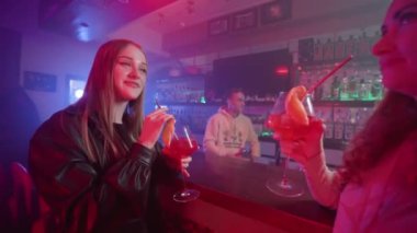İki Kız Arkadaş Bir Neon Işıklandırma Gece Kulübü 'nde Barın Yanında Ellerinde Kokteyllerle Dans Ediyor. Gece Barındaki Partide Eğlenen Mutlu Kadınlar. Yavaş Hareket.