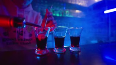 Guy Barmen, Blue Neon Lighting 'deki bir barın üzerinde üç şeffaf bardağa alkollü kokteyl dolduruyor. Bir gece kulübünde eğlence ve eğlence kavramı. Yavaş Hareket.
