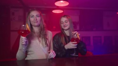İki Kız Arkadaş Bir Neon Işıklandırma Gece Kulübü 'nde Barın Yanında Ellerinde Kokteyllerle Dans Ediyor. Gece Barındaki Partide Eğlenen Mutlu Kadınlar. Yavaş Hareket.