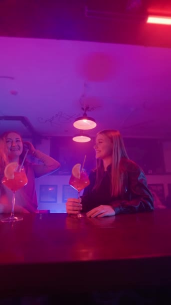 Две Счастливые Женщины Разговаривают Ночном Баре Неоновом Освещении Пьют Алкогольные — стоковое видео