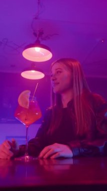 Neon Lighting and İçen Alkolik Kokteyller 'de Bir Gece Barında Konuşan İki Mutlu Kadın Arkadaş. Gece kulübü ve Kadın Arkadaşlığı kavramları. Ağır çekim. Dikey Video.