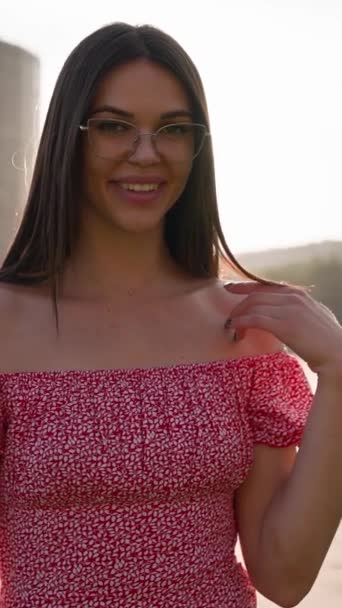 若い大人の笑顔の女性は 日没の間 街の公園を通って眼鏡とピンクの服を着ています 春の時間と世界の女性の日 ビジョンメガネコンセプト 垂直ビデオ スローモーション — ストック動画