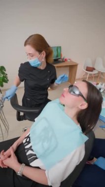 Diş teli takan genç yetişkin kadın klinikte kadın diş hekimi ve bakımı için reçete yazan bir asistan tarafından muayene ediliyor. Diş Sağlığı ve Tıp Konsepti. Yavaş Hareket, Dikey Video.
