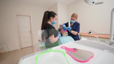 Üniformalı ve Tıbbi Maskeli Genç Yetişkin Dişçi Modern Diş Kliniğinde Diş Tedavisini Çözüyor. Sağlık ve Tıp Konsepti 'nden. Yavaş Hareket.