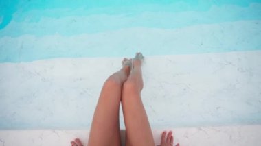 Top View, Slender Woman havuzun kenarına oturur ve ayaklarını yere vurur. Zayıflamış ve zayıflamış vücut kavramı. Ayak Sağlığı. Güzel Dişi Bacaklar. Tanınmayan kişi. Yavaş Hareket.