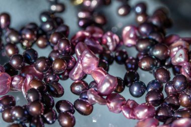 Şeffaf cam bir yüzey üzerinde, doğal kusurları olan koyu pembe bir barok inci kolyenin makro soyut dokusu