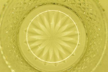 This image shows a macro abstract texture background of a round translucent lead crystal glass surface with a starburst design and diamond cuts, in the color of yellow.