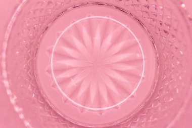 This image shows a macro abstract texture background of a round translucent lead crystal glass surface with a starburst design and diamond cuts, in the color of pink.