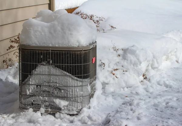 Close up view of an exterior home air conditioning unit, covered with deep snow following a winter blizzard