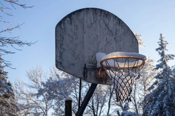 stock image Close up abstract view of a grungy old outdoor basketball hoop and backboard, containing snow from a recent blizzard with back lit sunlight