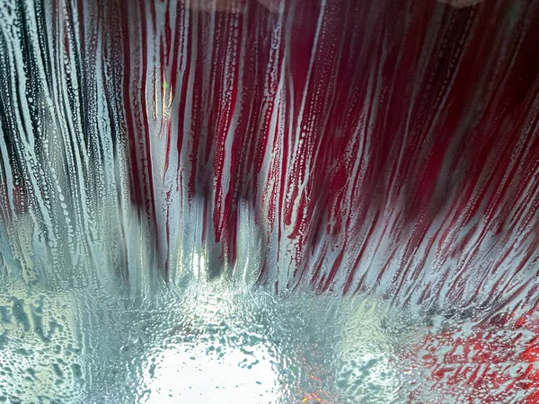 カラフルな石鹸と水滴のデザインで 自動洗車で車のフロントガラスの抽象的なテクスチャビューを閉じます — ストック写真
