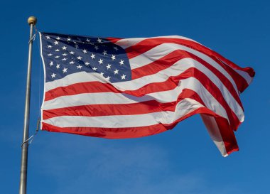 Mavi gökyüzü arka planında bayrak direğinde dalgalanan bir Amerikan bayrağının yakın görüntüsü