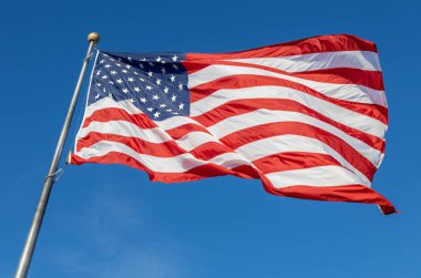 Mavi gökyüzü arka planında bayrak direğinde dalgalanan bir Amerikan bayrağının yakın görüntüsü