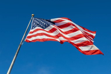 Mavi gökyüzü arka planında bayrak direğinde dalgalanan bir Amerikan bayrağının yakın görüntüsü