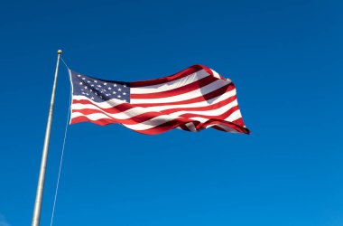 Mavi gökyüzü arka planında bayrak direğinde dalgalanan bir Amerikan bayrağının yakın görüntüsü
