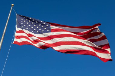 Mavi gökyüzü arka planında bayrak direğinde dalgalanan bir Amerikan bayrağının yakın görüntüsü
