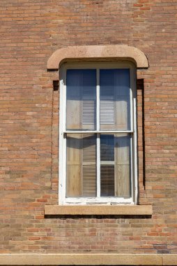 Eski bir turuncu ve bej tuğlalı ve yıpranmış tuğlalı duvarın dokusu, tuğla çerçeveli ahşap bir pencereye sahip.