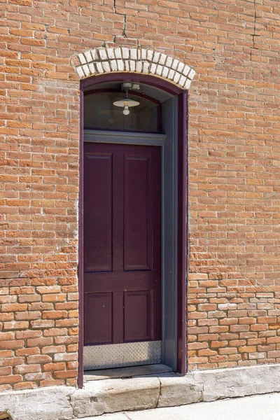 レンガ造りのアーチ型の入り口と暗い赤いドアを備えたみすぼらしいシックな古い風化した粘土レンガの壁のテクスチャの背景を閉じます — ストック写真