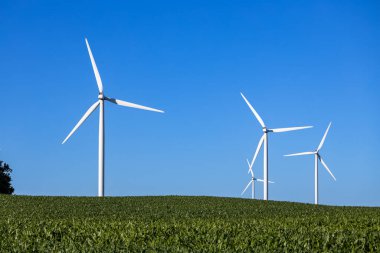 Berrak mavi gökyüzünün altındaki tarımsal alanda kopyalanmış devasa rüzgar türbinlerinin tam kare manzara görüntüsü.