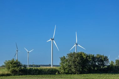 Berrak mavi gökyüzünün altındaki tarımsal alanda kopyalanmış devasa rüzgar türbinlerinin tam kare manzara görüntüsü.
