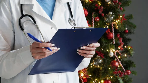 코트를 청진기를 의사는 아름답게 장식된 크리스마스 트리를 배경으로 알약을 스톡 이미지