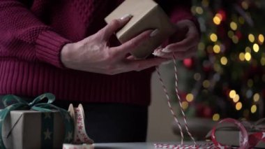 Burgundy süveter giyen yakın plan bir sürü hediye paketi içinde güzel kağıt ve kurdeleler, bir Noel ağacının arka planında fiyonklar. Noel, yeni yıl tatili, hediye paketi.