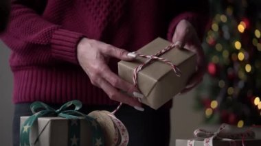 Burgundy süveter giyen yakın plan bir sürü hediye paketi içinde güzel kağıt ve kurdeleler, bir Noel ağacının arka planında fiyonklar. Noel, yeni yıl tatili, hediye paketi.