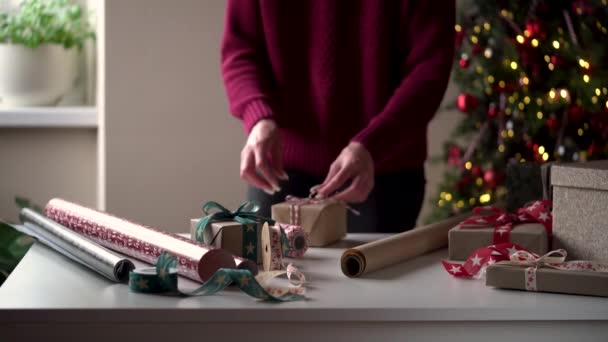 Gros plan femme dans un pull bordeaux emballe beaucoup de boîtes avec des cadeaux en beau papier et des rubans, des arcs sur le fond d'un arbre de Noël.Préparation pour Noël, vacances du Nouvel An, emballage cadeau