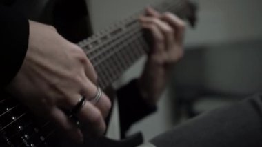 Kızın ellerinin yüzüklerle yakın çekimi siyah elektro gitarla melodi çalar. Bir sanatçının, rock müzisyeninin performansı. Tellerin Macro videosu, müzik enstrümanının detayları. Karanlık arka plan, seçici odaklanma.