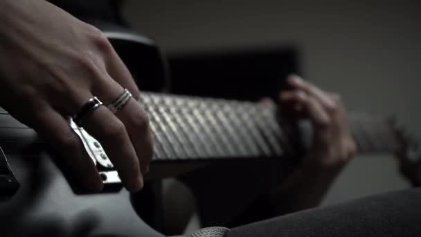 女孩手挽着戒指的特写在黑色电吉他上弹奏旋律 摇滚歌手的独奏 弦乐的宏观录像 乐器的细节 黑暗背景 选择性聚焦 — 图库视频影像
