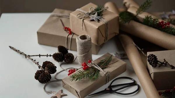 Zero waste and eco friendly christmas concept.Christmas and New Year gifts for family and friends wrapped in brown paper,rope and natural plant decor,tree branches,cones,berries,stars.Selective focus