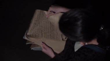  Gözlüklü esmer bir kızın yakın plan çekimi elinde kağıt tutarak yazı, yazı, takla, kağıt kırıntıları, üst görünüm, yavaş çekim videosu yazıyor. Güzel retro video.