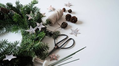 Noel çelengi kapısı, yıldızlarla süslenmiş doğal Noel ağacı dalları, koniler, makas ve kurdeleler beyaz masa, üst görünüm, kopyalama alanı. Ev için Noel çelengi yapma kavramı..