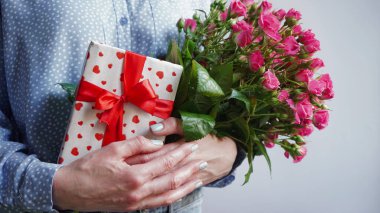 International Women's Day.Concept of greeting banner for international women's day on March 8.Close-up of girl's hands holding gift box and large bouquet of pink roses on gray background,copy space