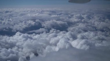 Açık güneşli bir günde, uçak kanadı, mavi gökyüzü üzerinde beyaz pofuduk bulutların üzerinde uçak penceresinden görüntü. Uçakla seyahat, iş uçuşları. Güzel 4K doğa videosu, yavaş çekim.