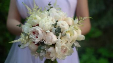 Beyaz elbiseli gelin elinde güzel bir buket beyaz şakayık, astilbe, okaliptüs yeşil ağaçların arka planında. Düğün çiçekçisi, gelin buketi, narin çiçek..