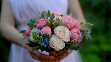 Beyaz elbiseli gelin elinde pembe şakayık buketi, güller, yeşil ağaç parkının arka planına karşı Oxypetalum. Düğün çiçekçisi, gelin buketi, kırılgan çiçek..