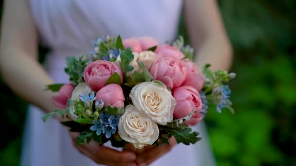 新娘身穿白色婚纱 手里拿着漂亮精致的结婚花束 粉红色的牡丹 氧气花瓣 衬托在绿树旁 婚礼花束 新娘的花束 脆弱的花朵 — 图库视频影像