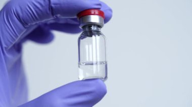 Mavi eldivenli doktorların yakın çekimlerinde grip, diyabet, koronavirüs, COVID-19 ve diğer hastalıklara karşı cam serum şişesi bulunur. Aşı kavramı, laboratuvar araştırması. Yeni ilaçlar icat et.