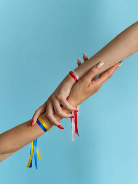 Women\'s hands with tied ribbons in colors of flag of Ukraine and Poland on a light blue background. The concept of assistance and friendship of neighboring state to people of Ukraine, sister support