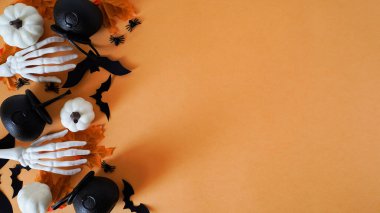 Yakın plan tatil dekoru: balkabakları, örümcekler, yarasalar, tencereler, insan iskelet elleri, turuncu bir arka planda sonbahar yaprakları ve gözleri, üst görünüm, kopya alanı. Cadılar Bayramı kutlaması konsepti, Cadılar Bayramı için tüm Cadılar Bayramı için dekor.