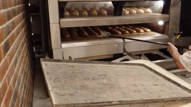 Fransız hamur işleri üreten küçük bir fırın. Fırıncı fırından taze pişmiş sıcak ekmeği çıkarır. Fırın ürünleri üretimi. Geleneksel Fransız ekmeği..